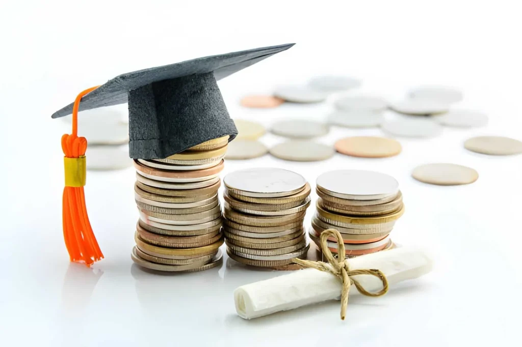 Tumpukan koin dengan topi wisuda dan gulungan ijazah di atas meja putih, menggambarkan biaya sertifikasi K3 terbaru 2026 sebagai investasi pendidikan dan pengembangan kompetensi profesional.