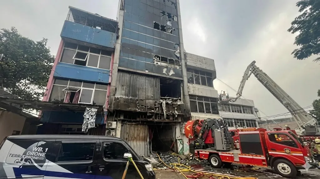 Situasi pasca kebakaran gedung Terra Drone di Jakarta Pusat, tampak bangunan bertingkat hangus terbakar dengan kaca pecah, dinding rusak parah, mobil pemadam kebakaran dan petugas damkar masih melakukan penyemprotan di lokasi.