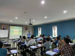 Pembinaan Ahli K3 PUBT di ruang kelas dengan instruktur menjelaskan materi menggunakan proyektor kepada peserta pelatihan yang duduk dan mengikuti sesi pembelajaran secara aktif.